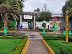 Entrada de la alcaldía Álvaro Obregón. Dos empleadas de la alcaldía platican. Una no utiliza cubrebocas porque está tomando un atole. Detrás de ellas, una lona de una convocatoria para inscribirse al servicio militar nacional; en medio, una lona de la Expo Café Álvaro Obregón, y a la derecha, dos mujeres con cubrebocas. Arriba de ellas una lona que dice “Adiós a los plásticos de un solo uso.” Canario, col. Tolteca, del. Álvaro Obregón. Fotografía del 28 de junio del 2021 por Ulises Felipe Chávez Valdovinos.