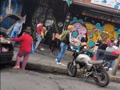 Padre con suéter rojo sin cubrebocas que carga a un bebé junto a su esposa que está abriendo el local. Ella tampoco usa cubrebocas; también hay un adulto con gorra amarilla que no usa cubrebocas, en el minuto 00:03:25 del video. Captura de pantalla por Ulises Felipe Chávez Valdovinos.