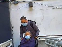 Mujer de la tercera edad con cubrebocas, en silla de ruedas, que es llevada por quien parece ser su hijo por la rampa de discapacitados, que es también el camino de salida, en el minuto 00:02:05 del video. Captura de pantalla: Ulises Felipe Chávez Valdovinos.