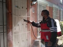 Un elemento de la cuadrilla de sanitización de la alcaldía Gustavo A. Madero sanitizando la entrada principal de un departamento de la unidad habitacional Plan de Iguala 69, ubicada en la colonia La Purísima Ticomán. Fotografía: César Omar Rojas Gómez.