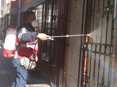 Un elemento de la cuadrilla de sanitización de la alcaldía Gustavo A. Madero sanitizando la entrada principal de un departamento de la unidad habitacional Plan de Iguala 69, ubicada en la colonia La Purísima Ticomán. Se puede observar la presión con la que es rociado el amonio cuaternario por a través del aspersor. Fotografía: César Omar Rojas Gómez.