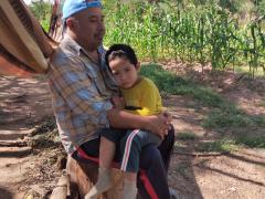 Felipe Chávez Isidoro y su nieto Dante, sentados en un tronco frente a una milpa. Fotografía 26 septiembre 2022.