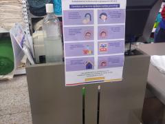 Cartel con medidas preventivas en el área de cajas junto con una botella de gel antibacterial, Tienda Bayon. Fotografía: Diana Elena Arredondo Linares