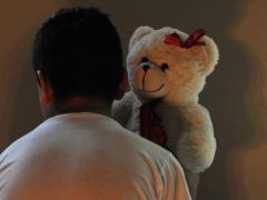 Niño de espalda, sentado frente a una pared mientras sostiene un oso de peluche. Fotografía: Mauricio Huizar.