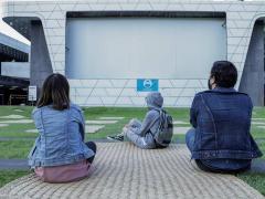 Tres personas frente a la pantalla del Foro al Aire Libre con distancia física entre ellos. Fotografia: Cineteca Nacional.