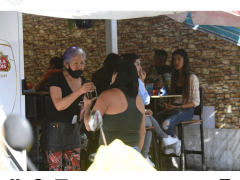 Local en Tepito de venta de alcohol, aún con restricciones acerca del aforo a estos establecimientos, las mesas tienen gente tomando bebidas. Al frente una mujer con cubrebocas mal puesto entrega una cerveza. Fotografía: Hugo García