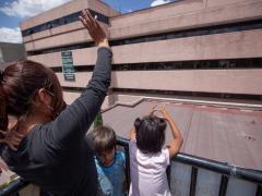 Mujer con dos niños saludan a lo lejos a alguien que está dentro del Hospital La Raza. Fotografía: @migueldimayuga.