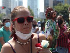Mujer carga figura de San Judas y flores, lleva cubrebocas en la barbilla. Al fondo feligreses, algunos llevan bien puesto el cubrebocas y otros no. Fotografía: @carlosodin89.