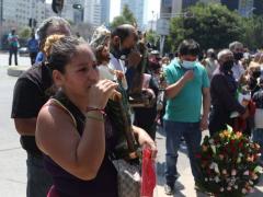 Feligreses a las afueras de la iglesia, hacen movimiento de persignación. En primer plano una mujer carga un San Judas sin cubrebocas, al fondo más gente, algunos con cubrebocas y otros sin él. Fotografía: @carlosodin89.