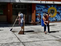 Tres señoras barren y recogen la basura restante del patio principal de una escuela, por Aarón Álvarez.