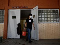 Hombre sujetando un balde de agua en la mano para realizar la limpieza dentro de las instalaciones de una escuela, por Aarón Álvarez.