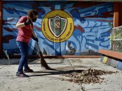 Mujer barriendo las hojas secas que cayeron en el patio principal de una escuela, por Aarón Álvarez.
