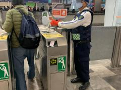 Policía toma temperatura a pasajero que ingresa al Metro y al fondo paletón del cartel “Callados prevenimos el contagio”, CdMx.