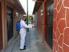 Hombre sanitiza la puerta de una casa color café, Iztapalapa. Fotografía: Stephanie Romero Faz.