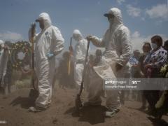 Fotografía de trabajadores con palas junto con asistentes a un entierro.