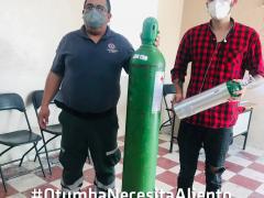 Hombre y joven con camisa a cuadros rojos y negros; en medio de ellos un cilindro de oxígeno. Fotografía: Gobierno de Otumba.