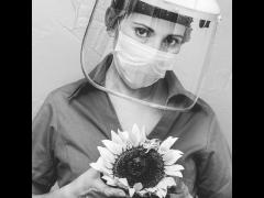 Enfermera con uniforme, cubrebocas y careta, entre las manos un girasol. Fotografía: Ruth Haro.