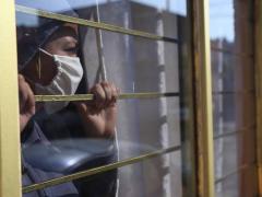 Mujer con cubrebocas asoma por una ventana, fotografía de Marina Luna.