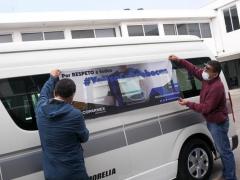 Un par de personas pegan calcomania en transporte público "Por respecto a todos #YoUsoCubrebocas", en Ruta Gris, Morelia, fotografía de Iván Villanueva.