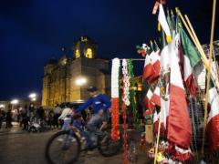 Joven en bicleta circula al lado de venta de objetos patrios. Fotografía: El Universal Oaxaca.