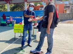 Un joven aplica gel a otro joven para ingresar al “mercadito” de Guelatao, Oaxaca. Fotografía: Facebook Agenda Oaxaca.