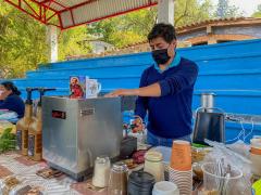 Hombre con cubrebocas prepara un café, “mercadito” de Guelatao, Oaxaca. Fotografía: Facebook Agenda Oaxaca.