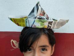 Briana posa con un sombrero de origami realizado con papel periódico, de un ejercicio tomado de una de las revistas para niños que están en venta en el puesto de periódico en el que trabaja su madre. Fotografía: Selene Ugalde.