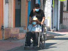 Mujer lleva a una persona mayor en silla de ruedas. Fotografía: Daniel Esquivel.