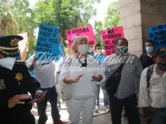 Empleados dialogan mientras muestran sus pancartas y hay un elemento de la policía a su lado. Fotografía: Diario de Yucatán.